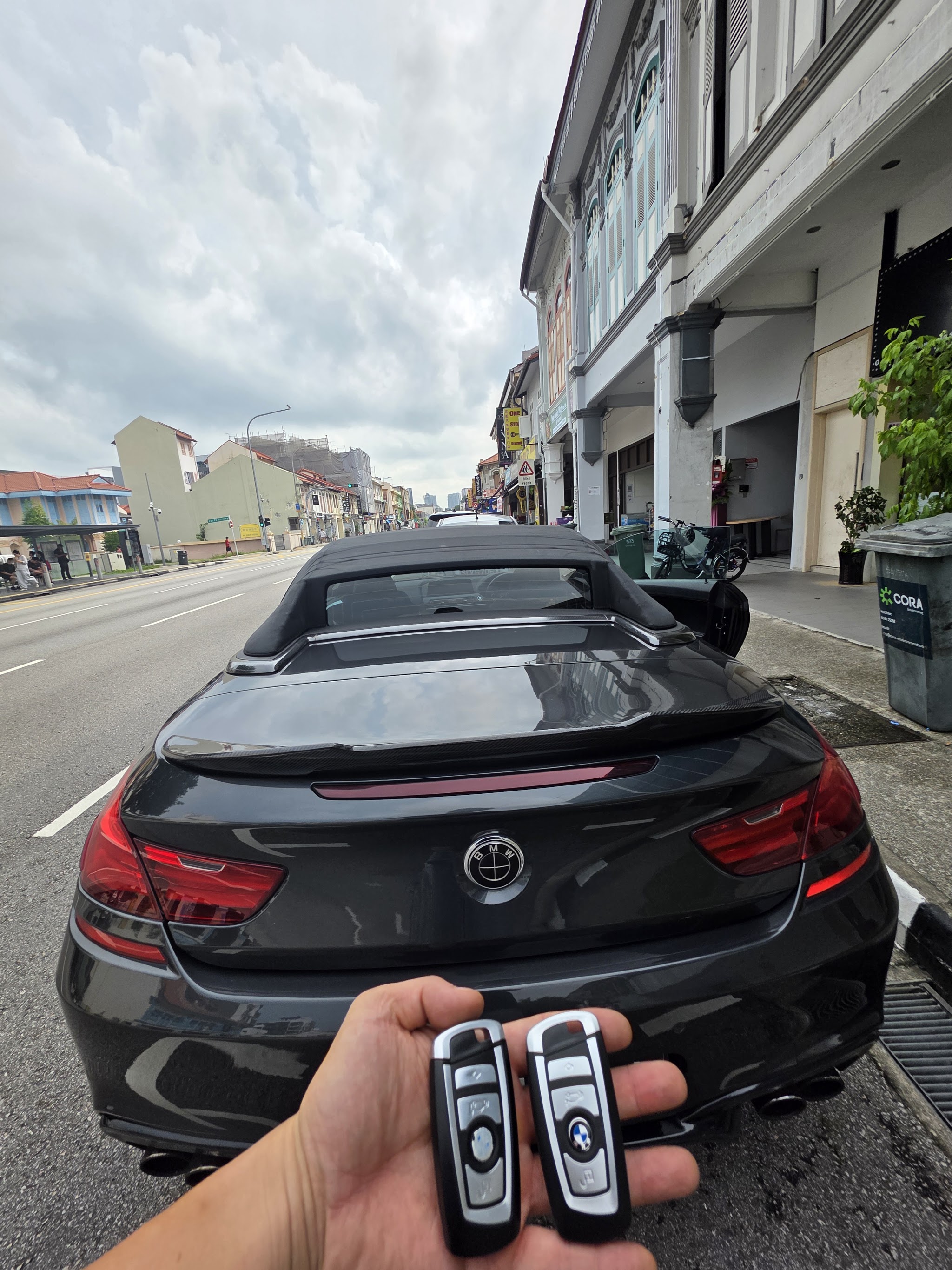Two BMW smart keys held in front of a black BMW convertible on Geylang Road