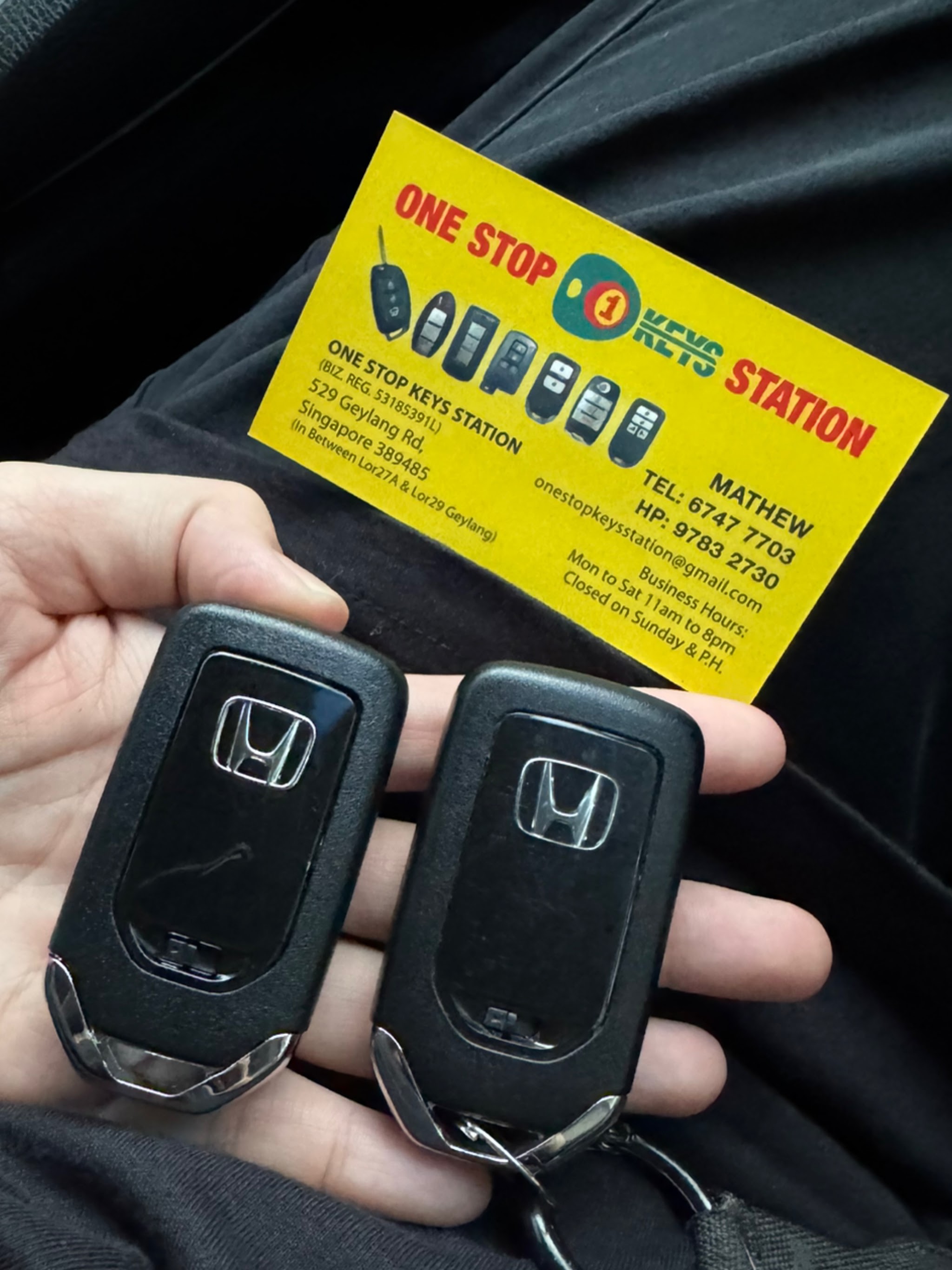 Two Honda smart keys held in a hand alongside the shop's printed business card